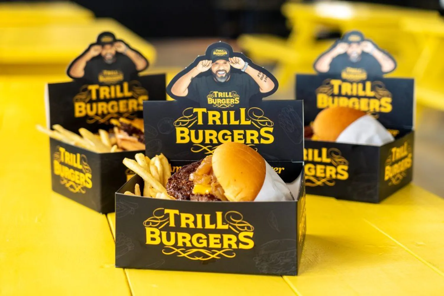 A row of Trill Burgers combo boxes on a yellow picnic table