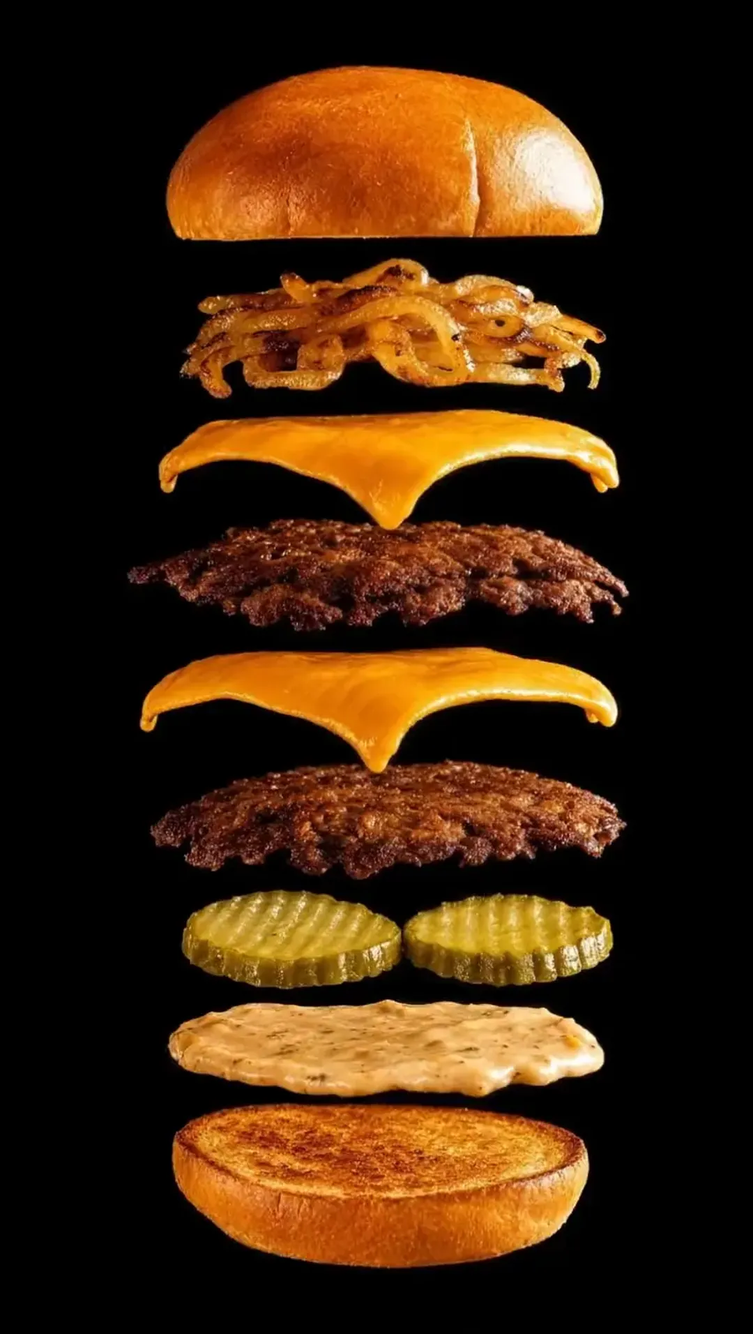 The OG Burger taken apart, its layers floating one above the other in the dark: the toasted potato roll, grilled caramelized onions, American cheese over a smashed patty, a second slice of cheese over a second patty, two pickles, Trill sauce, and the griddled bottom bun.
