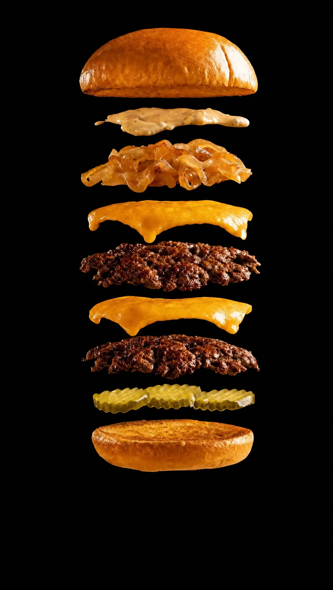 The OG Burger taken apart, its layers floating one above the other in the dark: the toasted potato roll, Trill sauce, caramelized onions, American cheese over a smashed patty, a second slice of cheese over a second patty, pickles, and the griddled bottom bun.