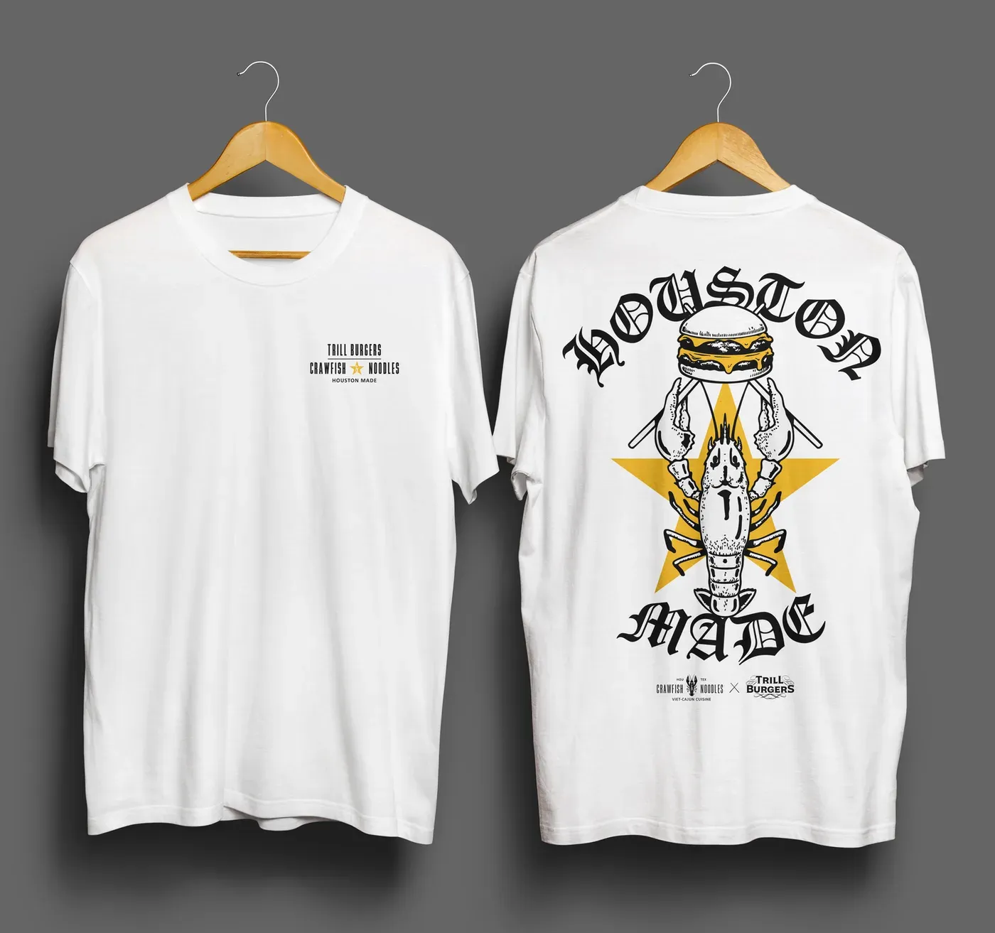 Front and back of a white t-shirt on wooden hangers against a grey backdrop. The front carries a small black chest lockup reading Trill Burgers above Crawfish and Noodles, with an ampersand set inside a yellow star, and Houston Made below. The back carries blackletter Houston arched above and Made curved below a crawfish drawn in black line that raises a cheeseburger in its claws over a large yellow star, with four bars radiating diagonally from behind it. Under the crest the Crawfish and Noodles logo and the Trill Burgers logo sit on either side of an X.